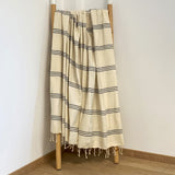 Fouta Calliope ecru noir 100% coton 190 g/m², légère et absorbante, idéale bain ou plage, au design rayé tendance et utilisable en paréo.