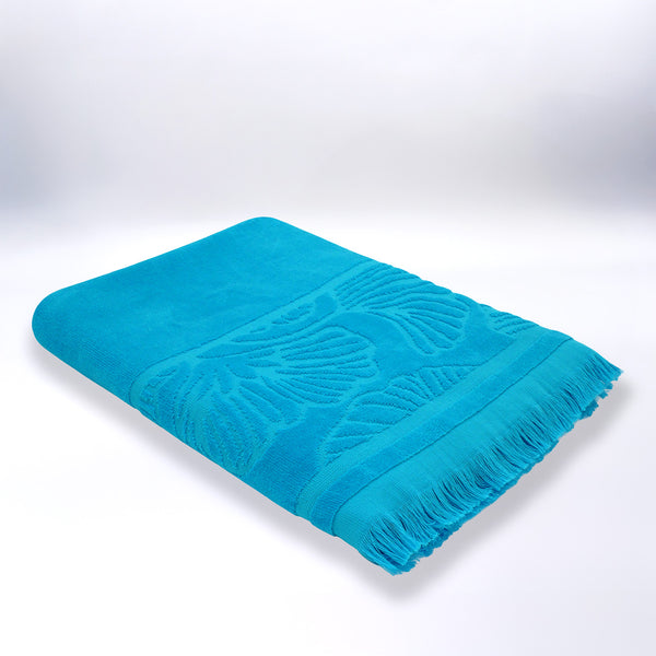 Serviette de plage ciselée bleue Kumini pliée, en velours jacquard doux et absorbant.