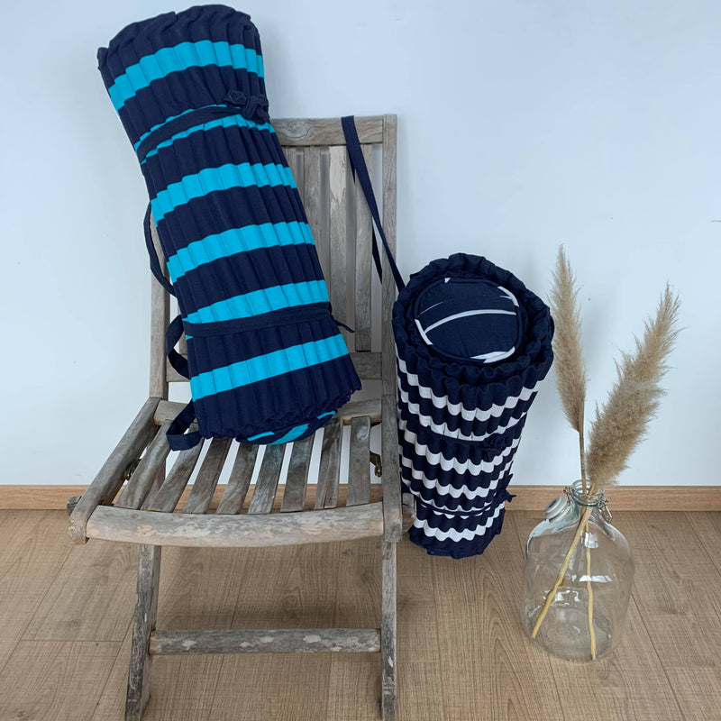 Matelas de plage rayé marine et turquoise . Facile à emporter grâce à sa bandoulière, ce matelas de plage apporte un super confort sur les plages de sable ou de galets . Avec ses rayures indémodables, il est idéal pour vos sorties à la plage ou sur votre transat au bord de la piscine. Très agréable grâce à sa qualité extérieure 100 % coton, il est également très confortable avec son coussin intégré. A shopper également sur le site les sacs et serviettes de plage coordonnés.